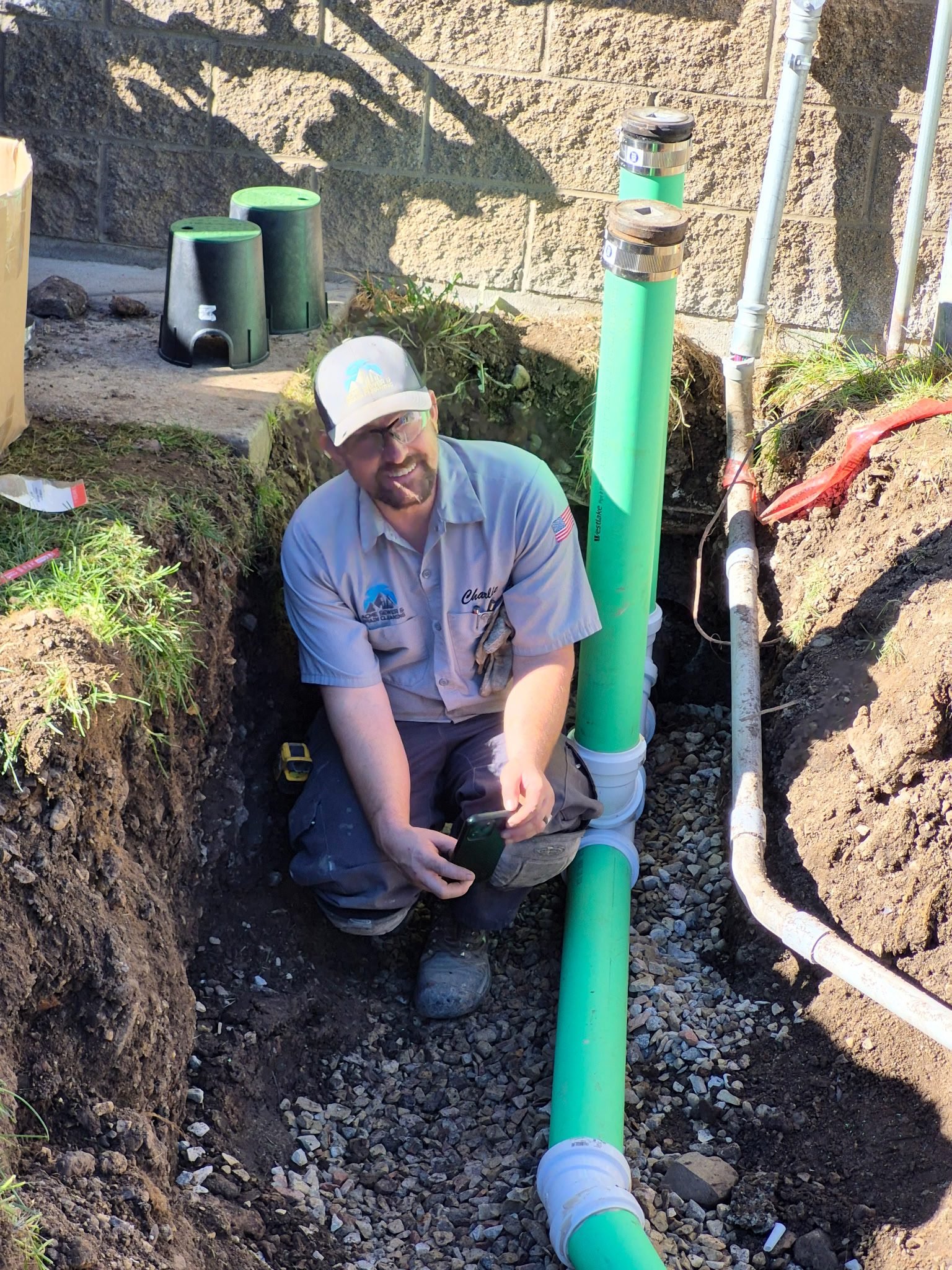 Capped green PVC cleanouts on a new sewer line in a trench at a commercial property